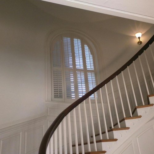 White plantation shutters decorating arched window located in round stairwell.